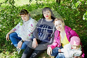 Three different funny women and one small seriously girl in the park full of apple blossom trees in a spring day. Aunts and niece