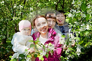 Three different funny women and one small seriously girl in the park full of apple blossom trees in a spring day. Aunts and niece