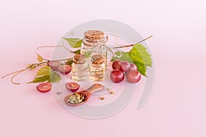 three different glass bottles with cork cap with natural organic grape seed oil on a pink background and a bunch of