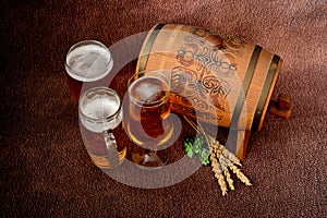 Three different glasses of light beer, ears of cereals, fruits of ripe hops and a wooden keg on a brown abstract background