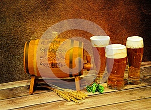 Three different glasses of light beer, a wooden barrel, ears of barley and hops on a wooden table