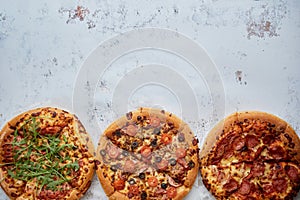 Three different kind of pizzas placed in a row on white rusty table