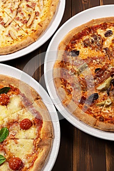 Three different pizzas on wooden background with tomato sauce, mixed cheese selection, ham and pork gyros