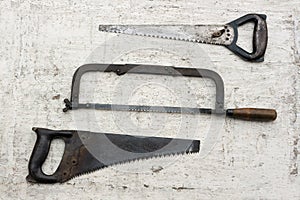 Three different used retro saws in white rustic wooden background