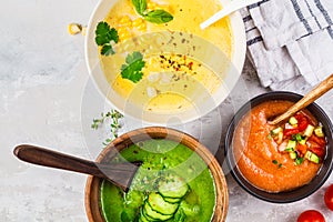 Three different vegetable cream soups in bowls on gray background. Corn, cucumber and gazpacho soups