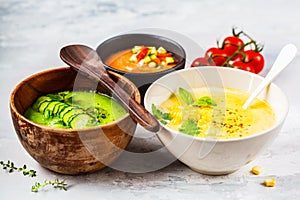 Three different vegetable cream soups in bowls on gray background. Corn, cucumber and gazpacho soups