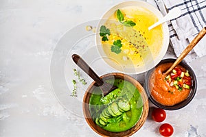 Three different vegetable cream soups in bowls on gray background. Corn, cucumber and gazpacho soups