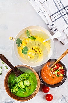 Three different vegetable cream soups in bowls on gray background. Corn, cucumber and gazpacho soups