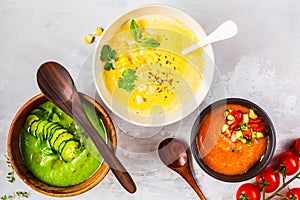 Three different vegetable cream soups in bowls on gray background. Corn, cucumber and gazpacho soups