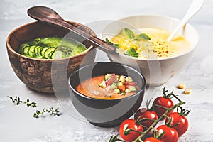 Three different vegetable cream soups in bowls on gray background. Corn, cucumber and gazpacho soups