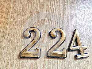 Three-dimensional brass numbers affixed to wood. Brass Numerals 224 Mounted on Wooden Surface photo