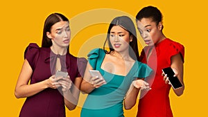 Three Dissatisfied Girls Holding Phones Reading Messages Over Yellow Background