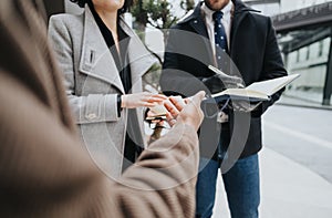 Three diverse business people engage in a discussion outdoors, standing near a potted pine tree, exchanging ideas via a