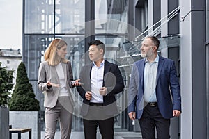 Three diverse business people walking and talking focused and thoughtful seriously outside office