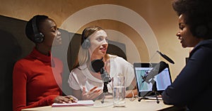 Three diverse female radio hosts wearing headphones talking on microphone for radio podcast