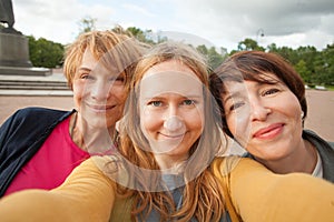 Three diverse happy women friends making selfie photo and having fun outdoors