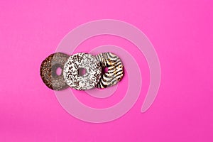 Three donuts with chocolate and icing on pink background. View from above