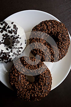 Three doughnuts on a white plate on a brown background