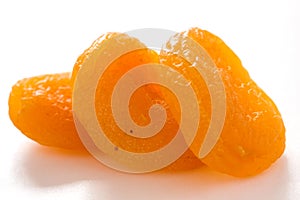 Three dried apricots on white surface