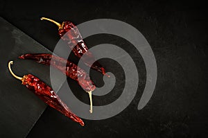 Three dried red hot chili peppers lie on a background of black concrete plaster and a stone cutting board. top view. beautiful