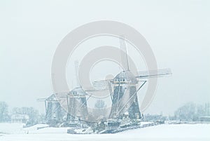 Three Dutch windmills during snowfall