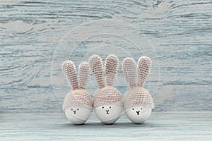 Three Easter eggs in crochet hats with bunny ears against painted shabby wooden background