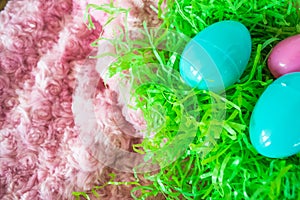 Three Easter eggs on green plastic grass and pink background