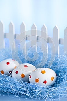 Three easter eggs in the nest and white fence