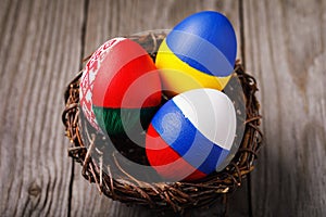 Three Easter eggs painted in colors of the flags of Ukraine, Belarus and Russia in the nest