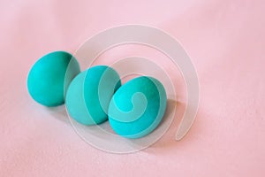 Three Easter eggs of turquoise color on a soft pink background.