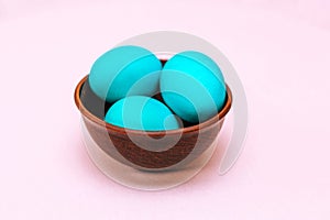 Three Easter eggs of turquoise color in a wooden plate on a soft pink background.