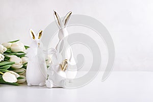 Three Easter rabbits figurines with bouquet of white tulips on white background. Easter celebration concept. Copy space. Front