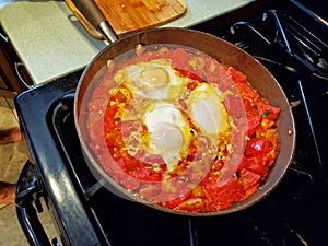 Three egg shakshuka cooking in an iron skillet on a stovetop