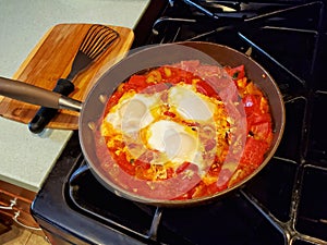 Three egg shakshuka cooking in an iron skillet on a stovetop