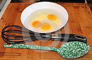 Three eggs in a bowl with a whisk and serving spoon