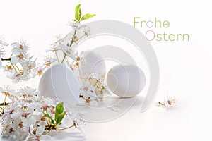 Three eggs and a branch of wild flowers on a white background germen text Frohe Ostern, meaning Happy Easter, holiday greeting