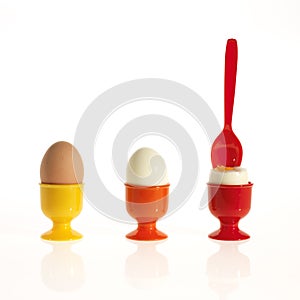 Three eggs in colorful egg cups with a spoon