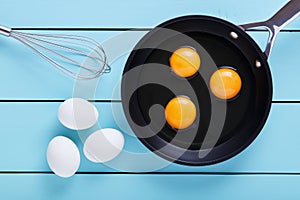 Three eggs cracked for frying in a frying pan with a whisker on table