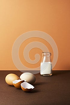 Three eggs with milk in glass bottle on brown background