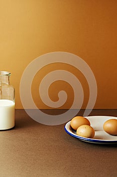 Three eggs with milk in glass bottle on brown background