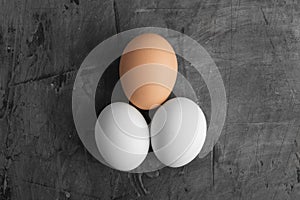 Three eggs, two white and one brown on a black background.