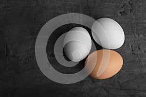 Three eggs, two white and one brown on a black background.