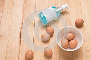 Three eggs in white cup and another egg put around a cup with ethyl alcohol hand gel a on a light brown wooden background, Top