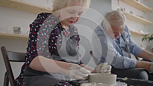 Three elderly people work on a potter's wheel in slow motion