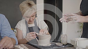 Three elderly people work on a potter's wheel in slow motion