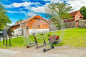 Three electric scooters stand on the grass in front of historical buildings in the old town of Oslo, Norway