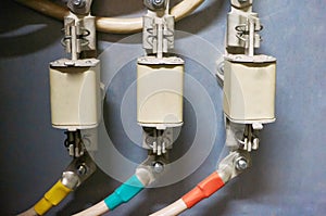 Three electrical high-voltage fuses connected to the colored wires. Industrial background.