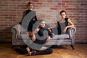 Three elegant latin women dancers in black dresses posing near sofa