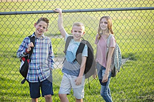 Three Elementary school students standing by a fence outside of their school