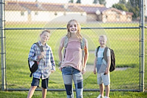 Three Elementary school students standing by a fence outside of their school